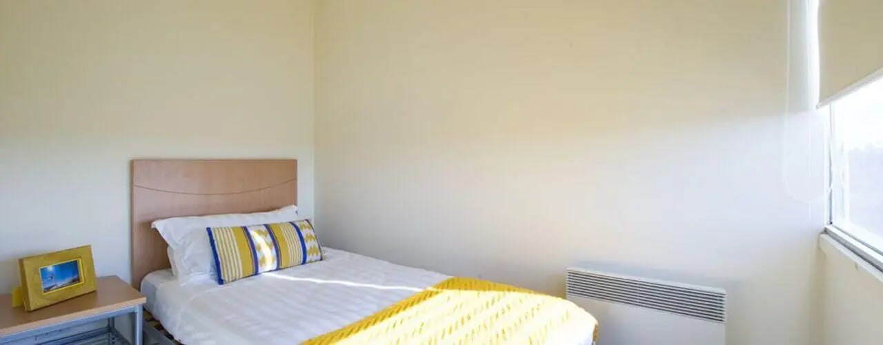Bed with white linen yellow blanket framed picture bedroom at Student Living - 550 Lygon in Melbourne Student Accommodation