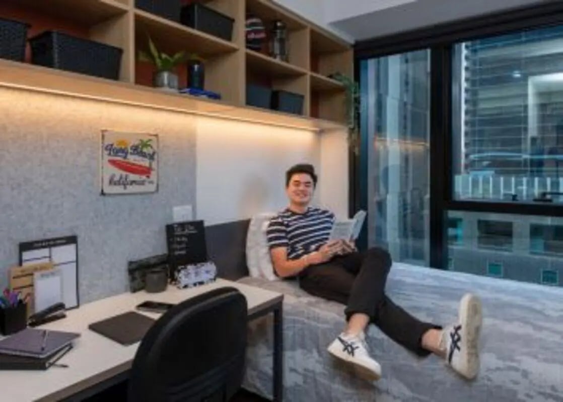 Young man reading on bed desk with shelves bedroom at UniLodge Melbourne Central in Melbourne Student Accommodation