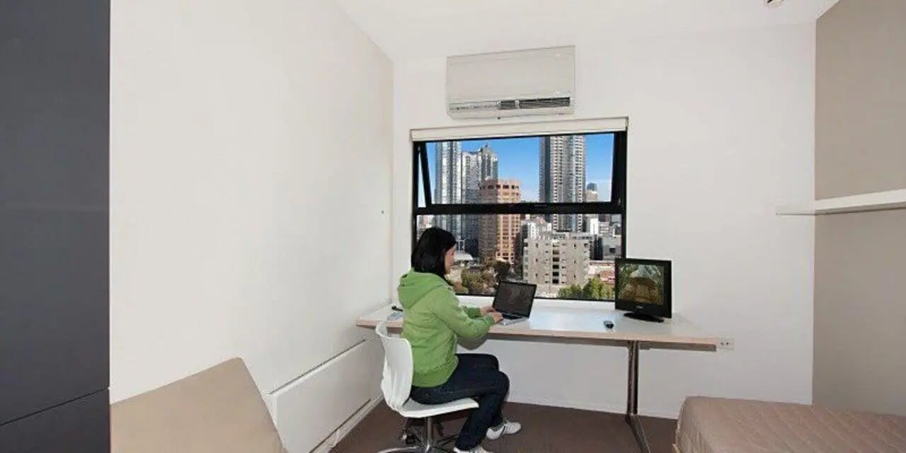 Woman working on laptop desk overlooking city study area at Student Living D1 in Melbourne Student Accommodation