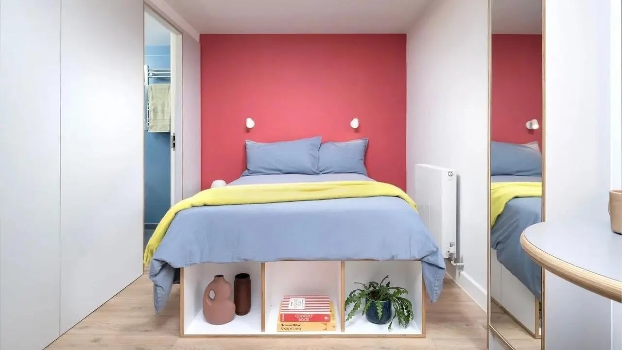 Bed with blue linens yellow throw bookcase bedroom at Scape Kings Cross in London Student Accommodation