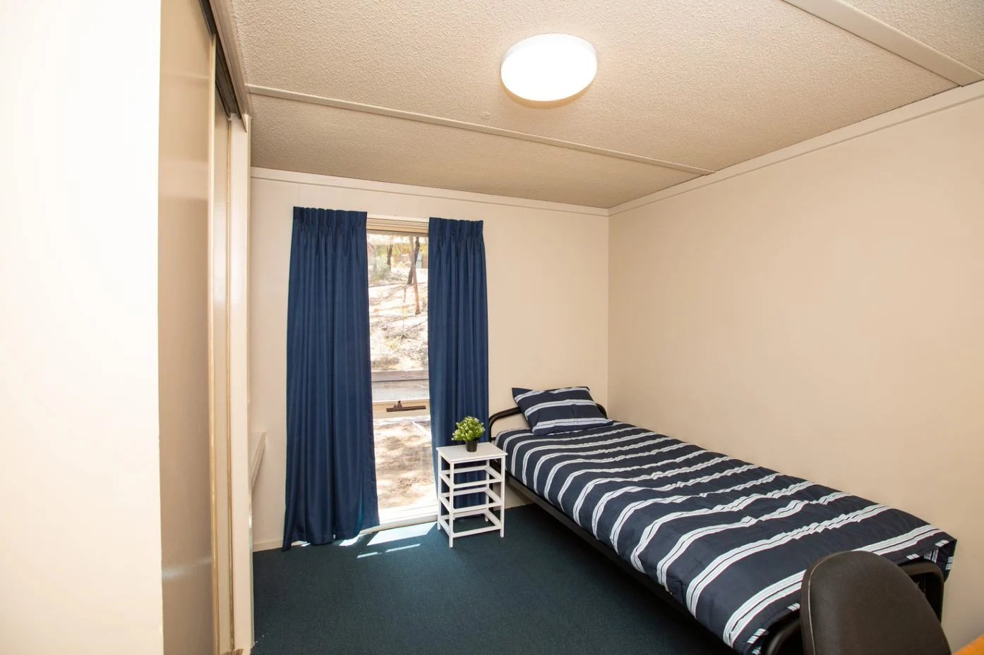 Single bed with striped bedding and bedside table bedroom at La Trobe University - Villas in Melbourne Student Accommodation