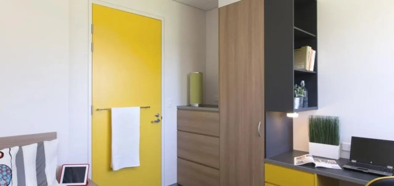 Desk shelving laptop plant door and towel bedroom at Western Sydney University Penrith Village in Sydney Student Accommodation