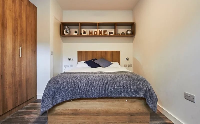 Bed with grey blanket wooden headboard shelves bedroom at City Heights - Cardiff in Cardiff Student Accommodation