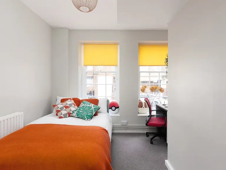 Bed desk red chair window with yellow blind bedroom at Louise House in London Student Accommodation
