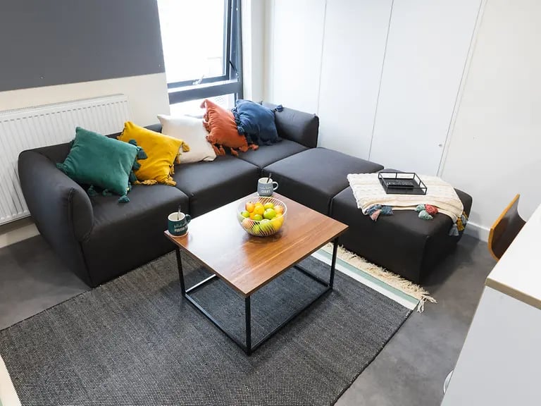 Dark sectional sofa with colorful pillows and coffee table living room at Oxford House - Newcastle in Newcastle Upon Tyne Student Accommodation