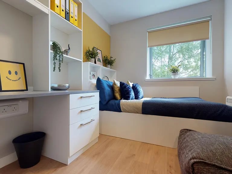 Desk shelves bed with blue pillows and plant bedroom at Centro House in Stirling Student Accommodation