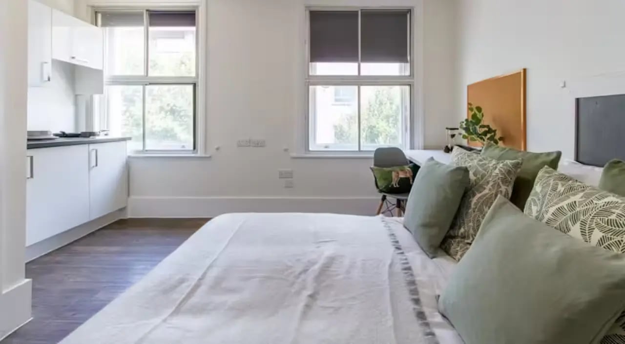 Bed with pillows kitchen area and desk Bedroom at Bloomsbury Janet Poole House in London Student Accommodation