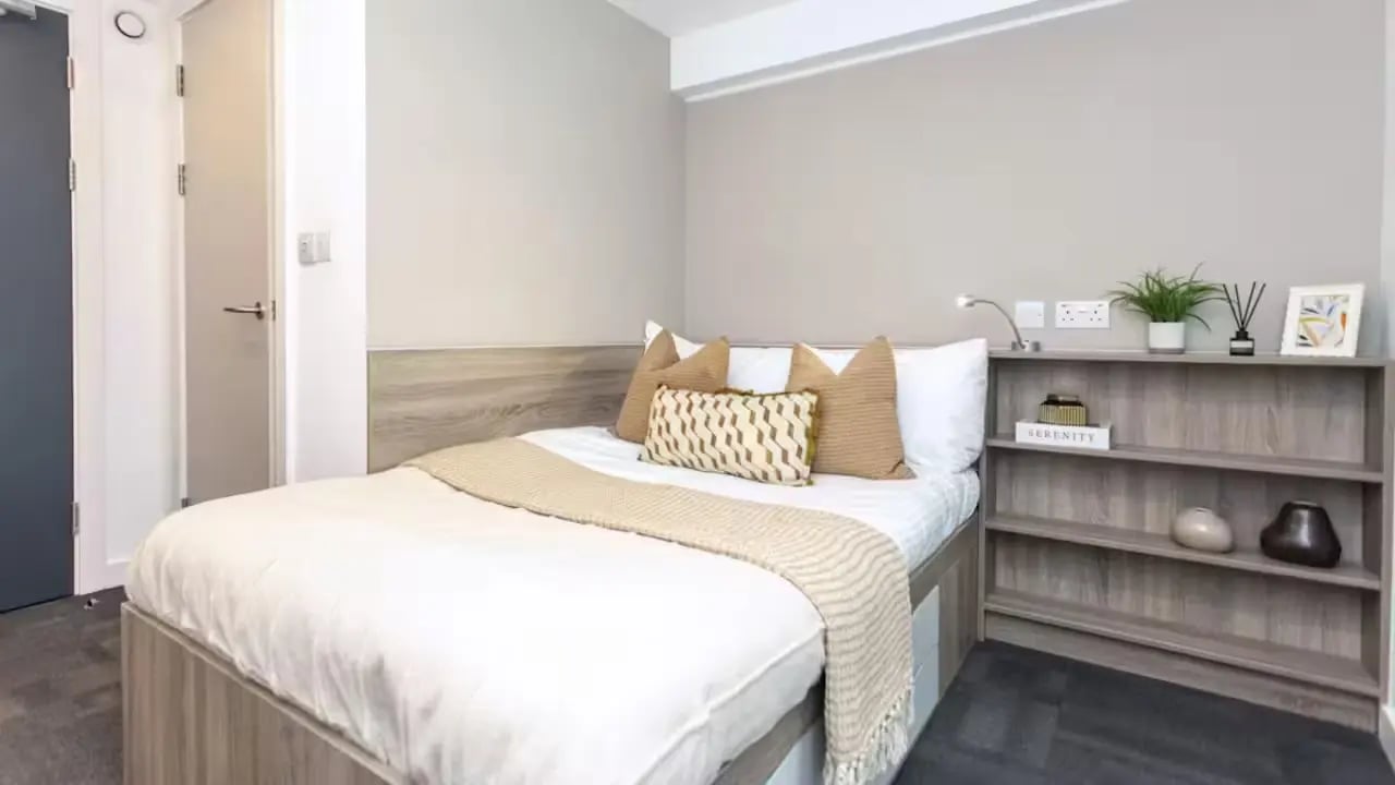 Bed with pillows and throw next to bookshelf bedroom at Gillows in Lancaster Student Accommodation