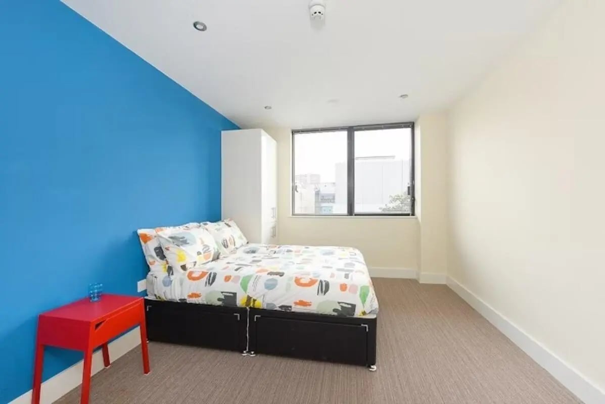 Bed with colorful bedding white wardrobe red nightstand bedroom at Hydrogen in Nottingham Student Accommodation