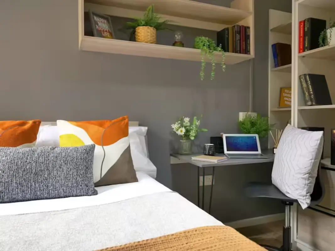 Bed with pillows desk with laptop and bookshelves bedroom at Emily Davies in Southampton Student Accommodation