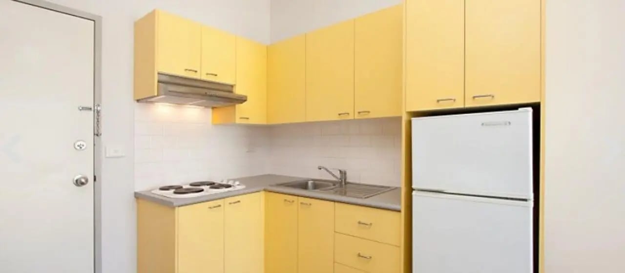 Yellow cabinets refrigerator stove sink kitchen at Student Living - 570 Swanston in Melbourne Student Accommodation