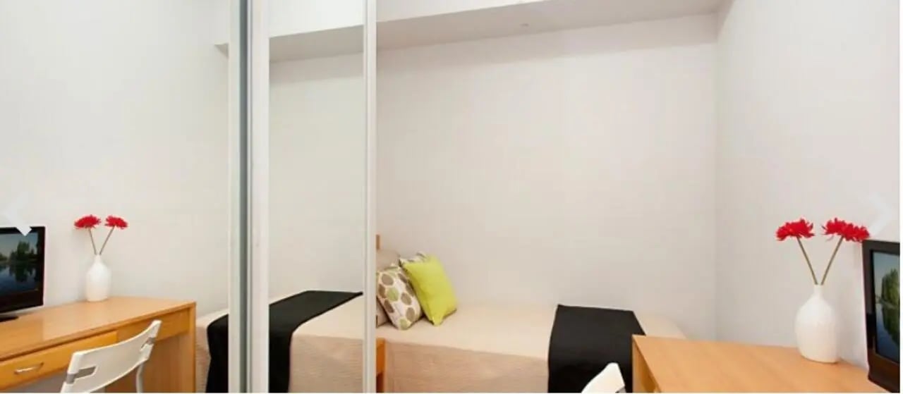 Bed with pillows desk chair and flowers bedroom at Student Living - 570 Swanston in Melbourne Student Accommodation