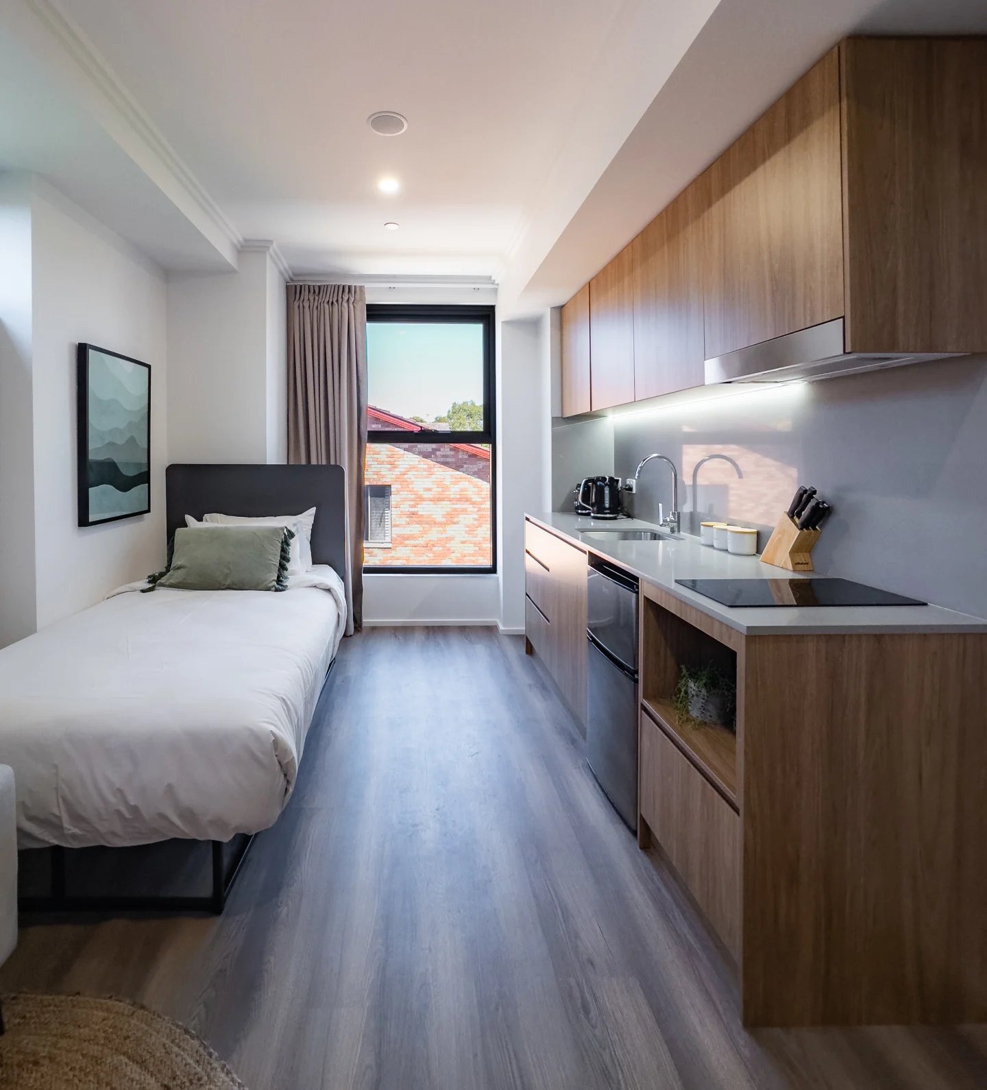 Bed with green pillow and modern kitchen studio at UKO Sutherland in Sydney Student Accommodation