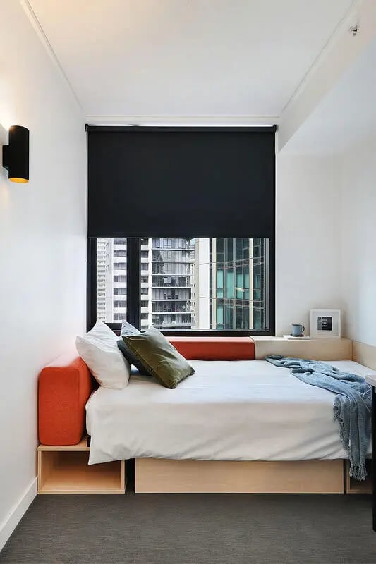 Bed with orange couch pillows window view Bedroom at Iglu Melbourne City in Melbourne Student Accommodation