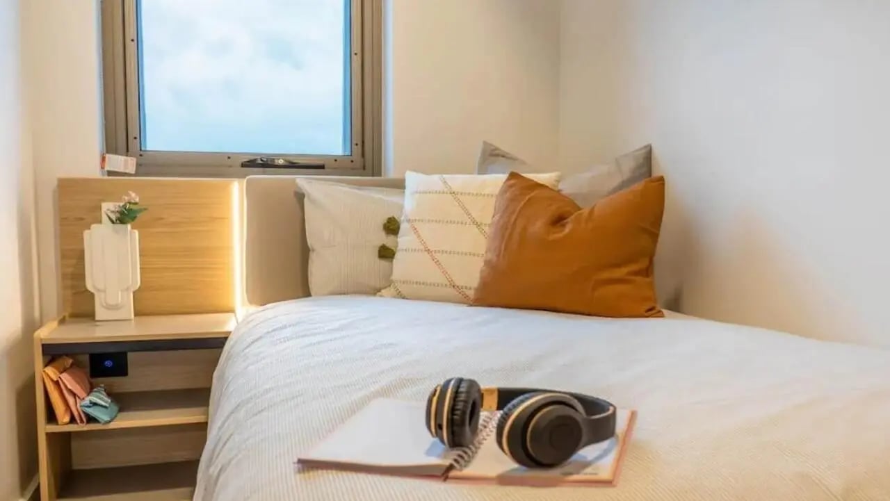 Bed with pillows headphones and notebook bedroom at The Switch Adelaide in Adelaide Student Accommodation