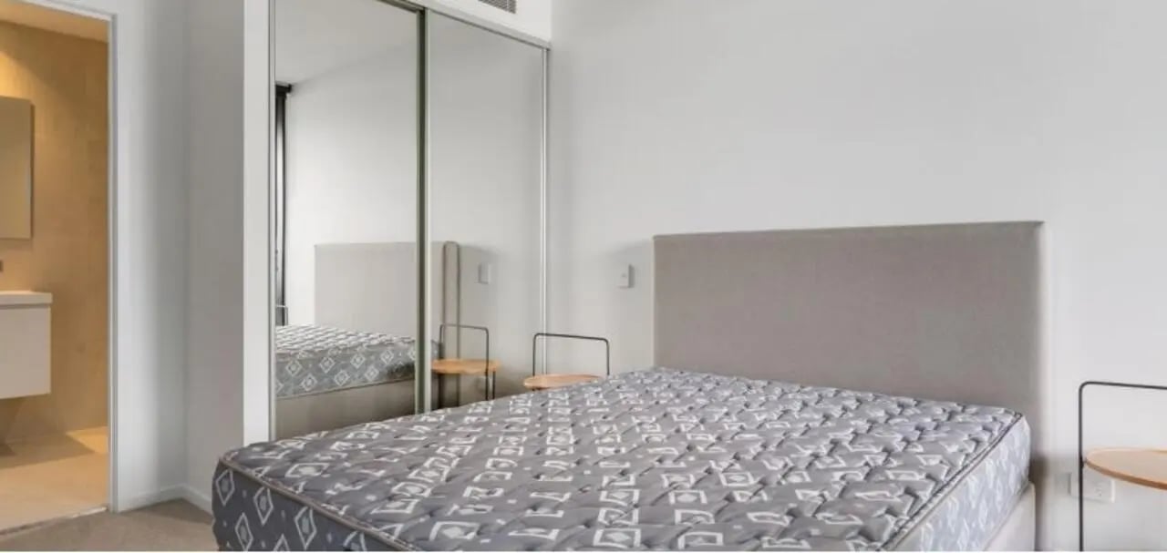 Bed with patterned mattress mirrored wardrobe bathroom entryway bedroom at Realm Kangaroo Point in Brisbane Student Accommodation