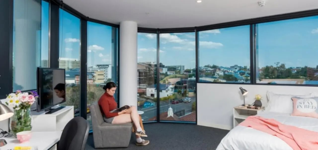Woman reading on chair by desk and bed bedroom at Unilodge South Bank in Brisbane Student Accommodation