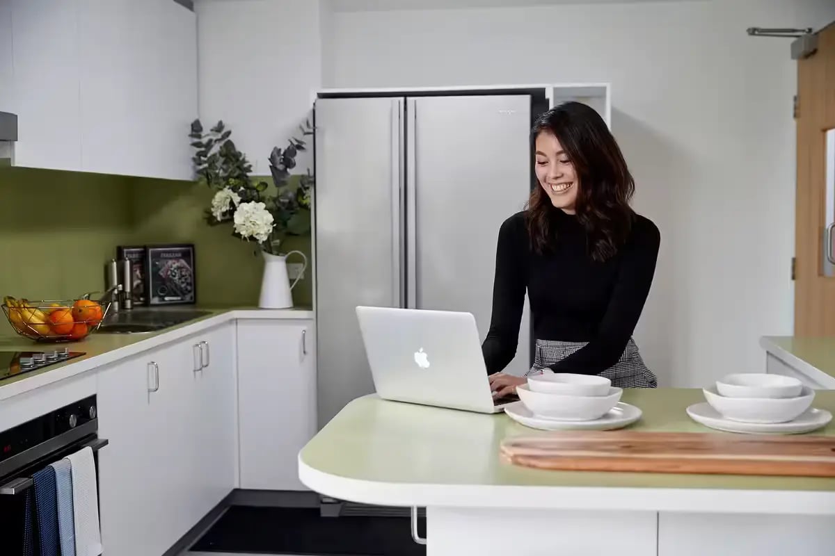 Woman using laptop at counter with bowls kitchen at Scape Tribune in Brisbane Student Accommodation
