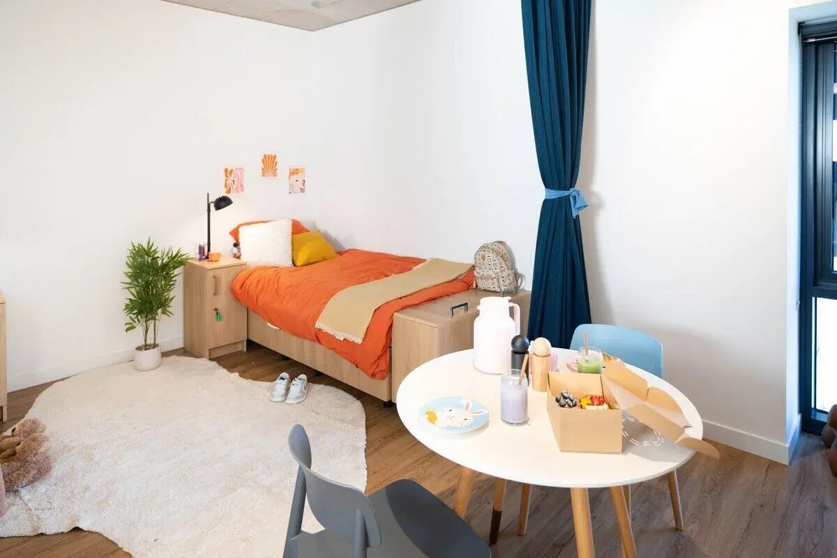 Orange bed white rug table and chairs bedroom at Scape Uni Square in Melbourne Student Accommodation
