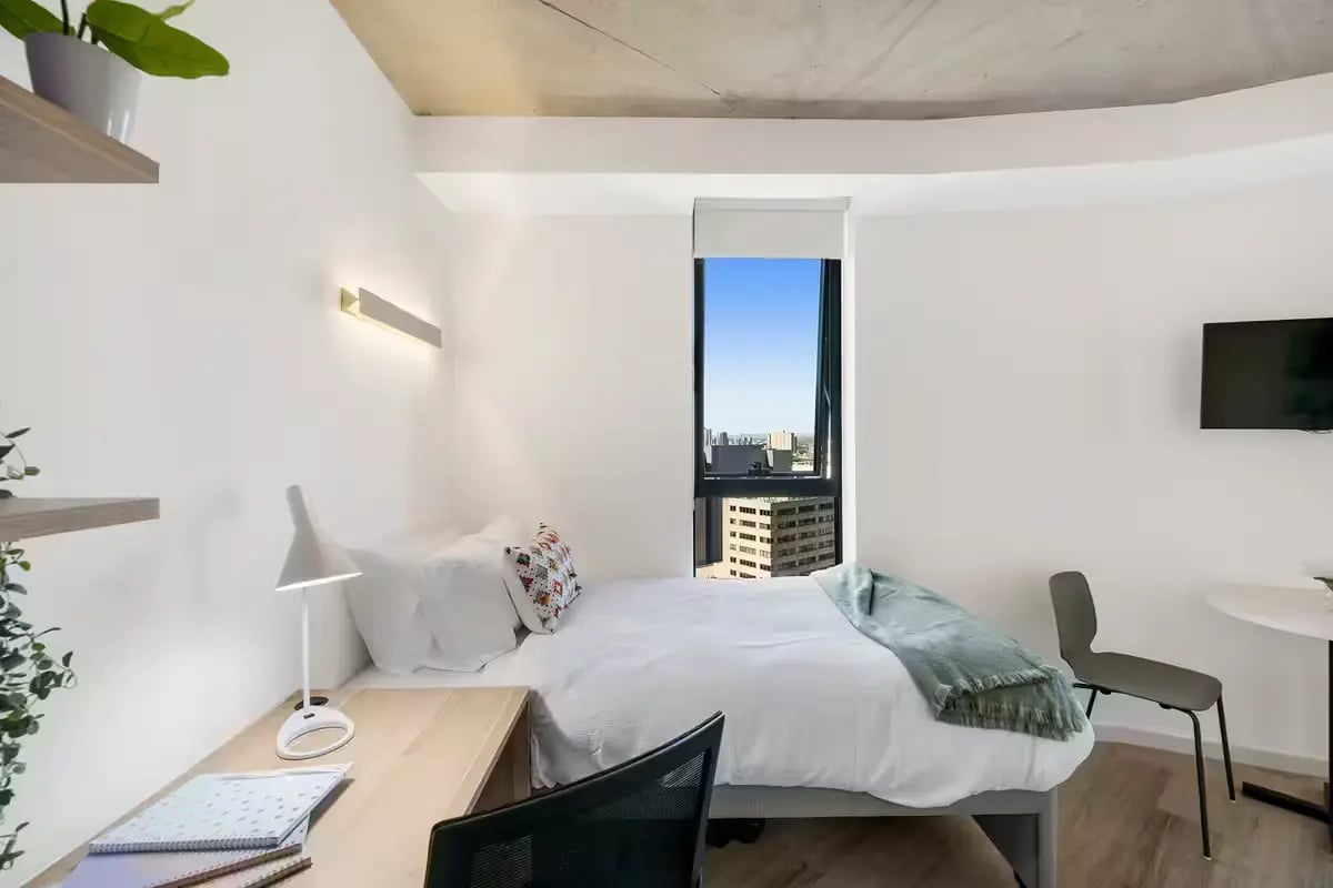 Bed desk chair and window with city view Bedroom at Scape Peel in Melbourne Student Accommodation