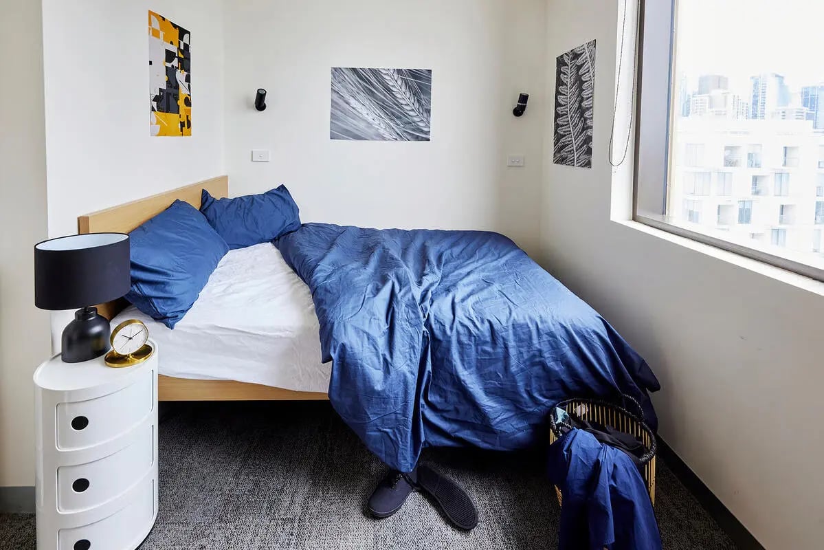 Bed with blue bedding nightstand lamp and artwork bedroom at Scape Queensberry in Melbourne Student Accommodation