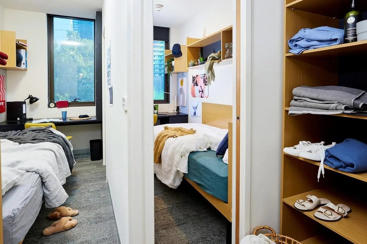 Two beds desk with black lamp and slippers Bedroom at Scape Queensberry in Melbourne Student Accommodation