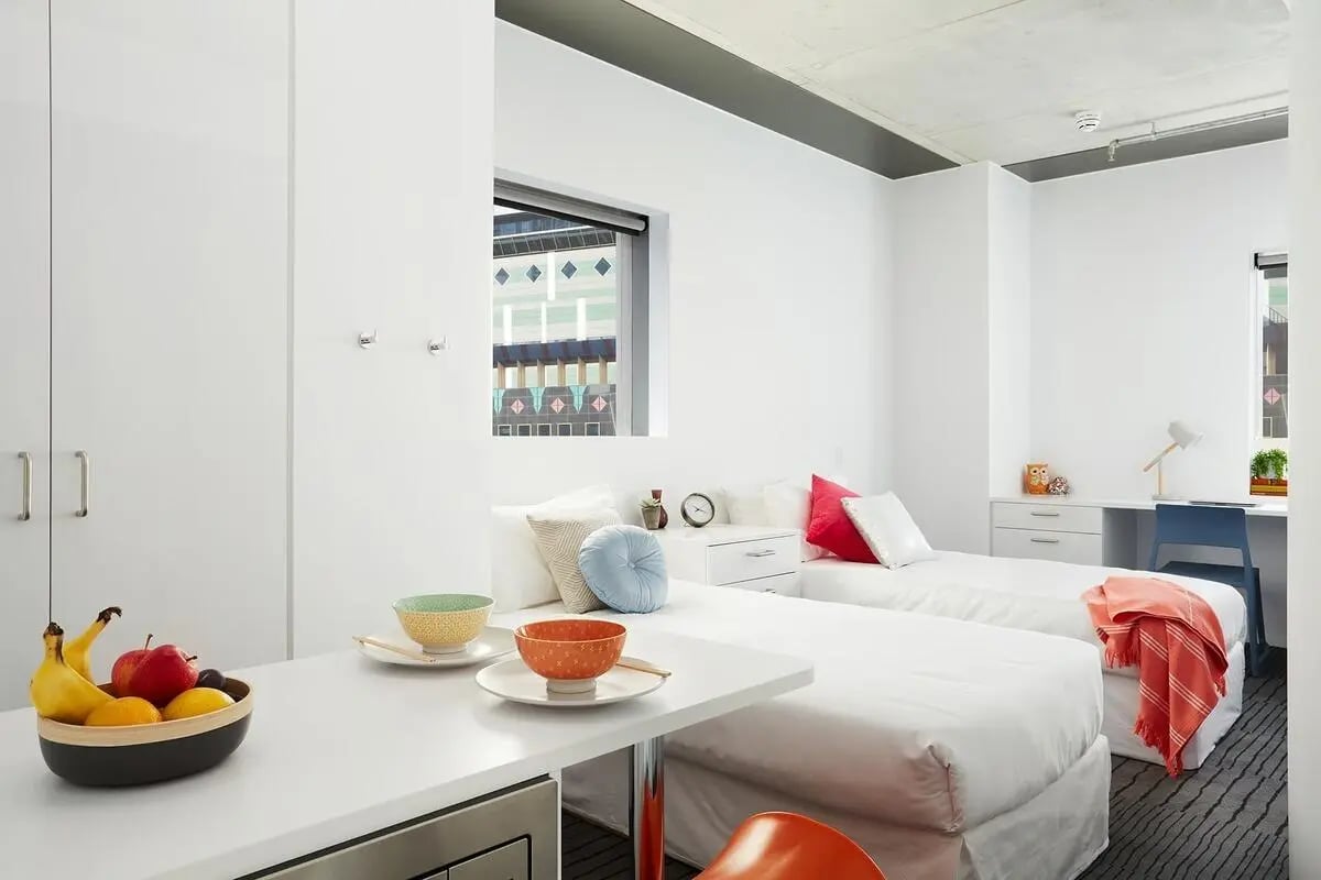 Two beds desk bowls fruit bedroom at Scape Swanston in Melbourne Student Accommodation