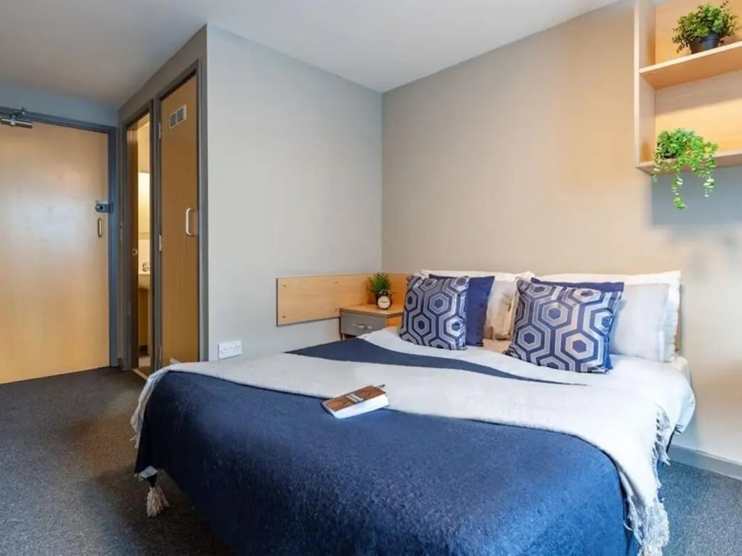 Bed with blue bedding pillows and shelves bedroom at Filbert Village in Leicester Student Accommodation