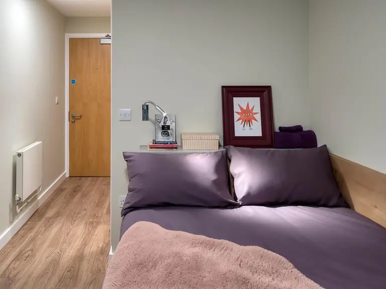 Bed with purple bedding wooden door radiator bedroom at The Curve in London Student Accommodation