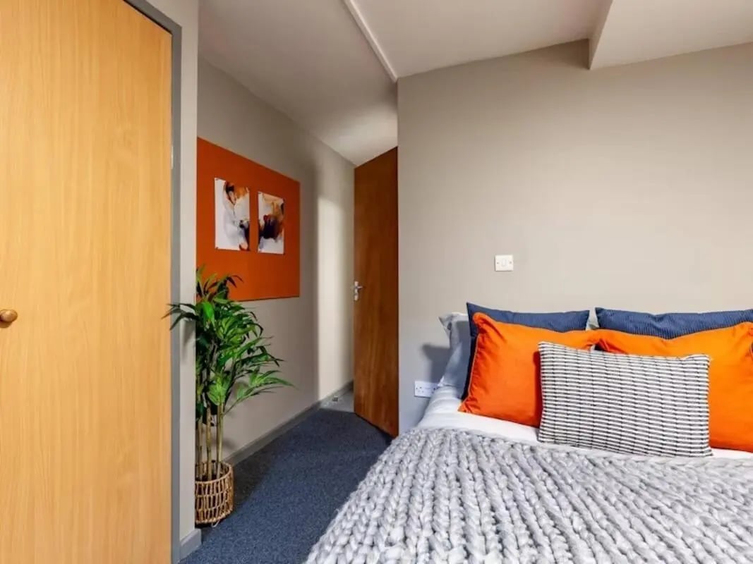 Bed with orange pillows and plant Bedroom at Devonshire Courtyard in Sheffield Student Accommodation