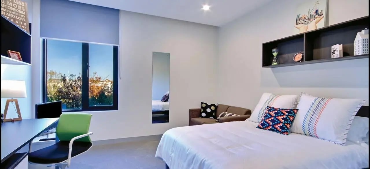 Bed desk couch pillows window bedroom at Scape Berkeley in Melbourne Student Accommodation