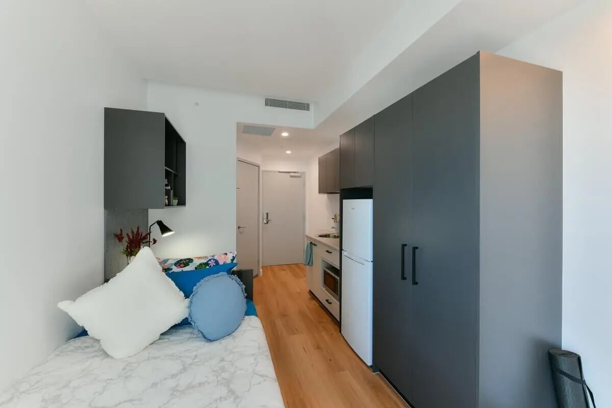 Bed with pillows kitchen area and wardrobe studio at UniLodge Toowong in Brisbane Student Accommodation