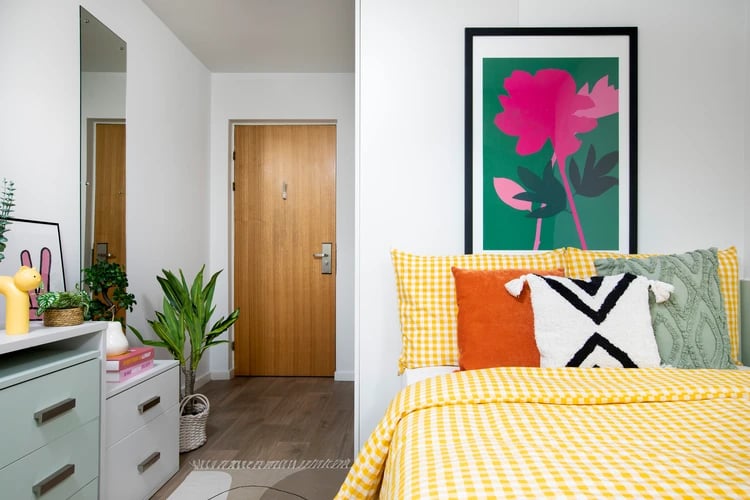 Bed with yellow gingham bedding and colorful pillows bedroom at Station Court in London Student Accommodation