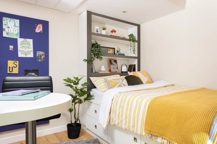 Bed with yellow stripes white bedding shelves and desk bedroom at Bridgewater Heights in Manchester Student Accommodation