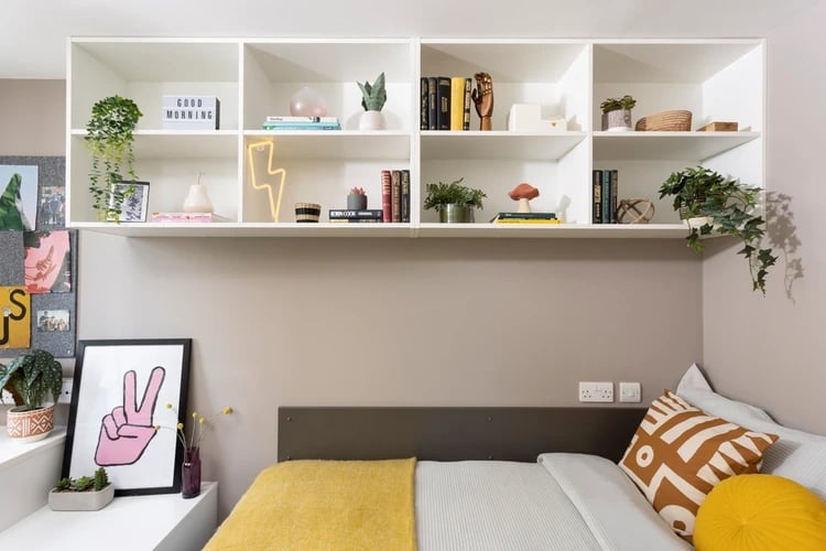 Bed with shelves above plants and artwork Bedroom at Stratford One in London Student Accommodation