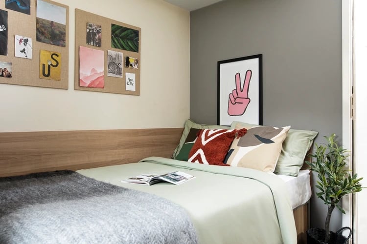 Bed with patterned pillows and corkboard bedroom at Elizabeth Croll House in London Student Accommodation
