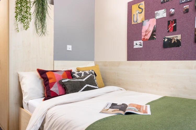 Bed with colorful pillows and open magazine Bedroom at The Plaza in Leeds Student Accommodation