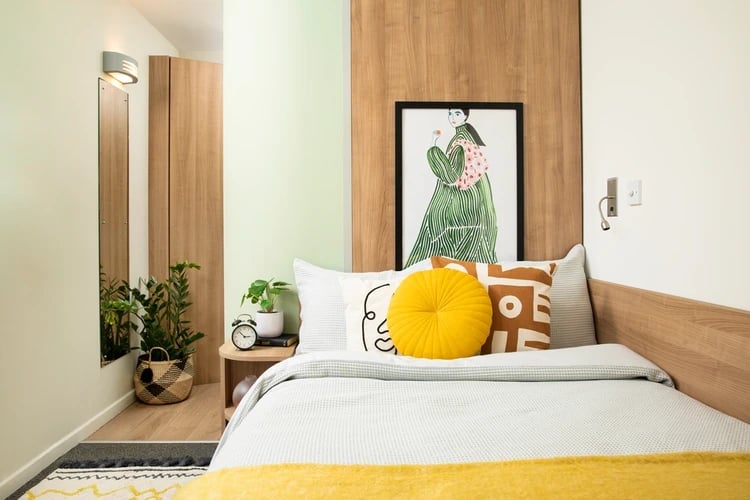 Bed with yellow cushion artwork alarm clock bedroom at Emily Bowes Court in London Student Accommodation