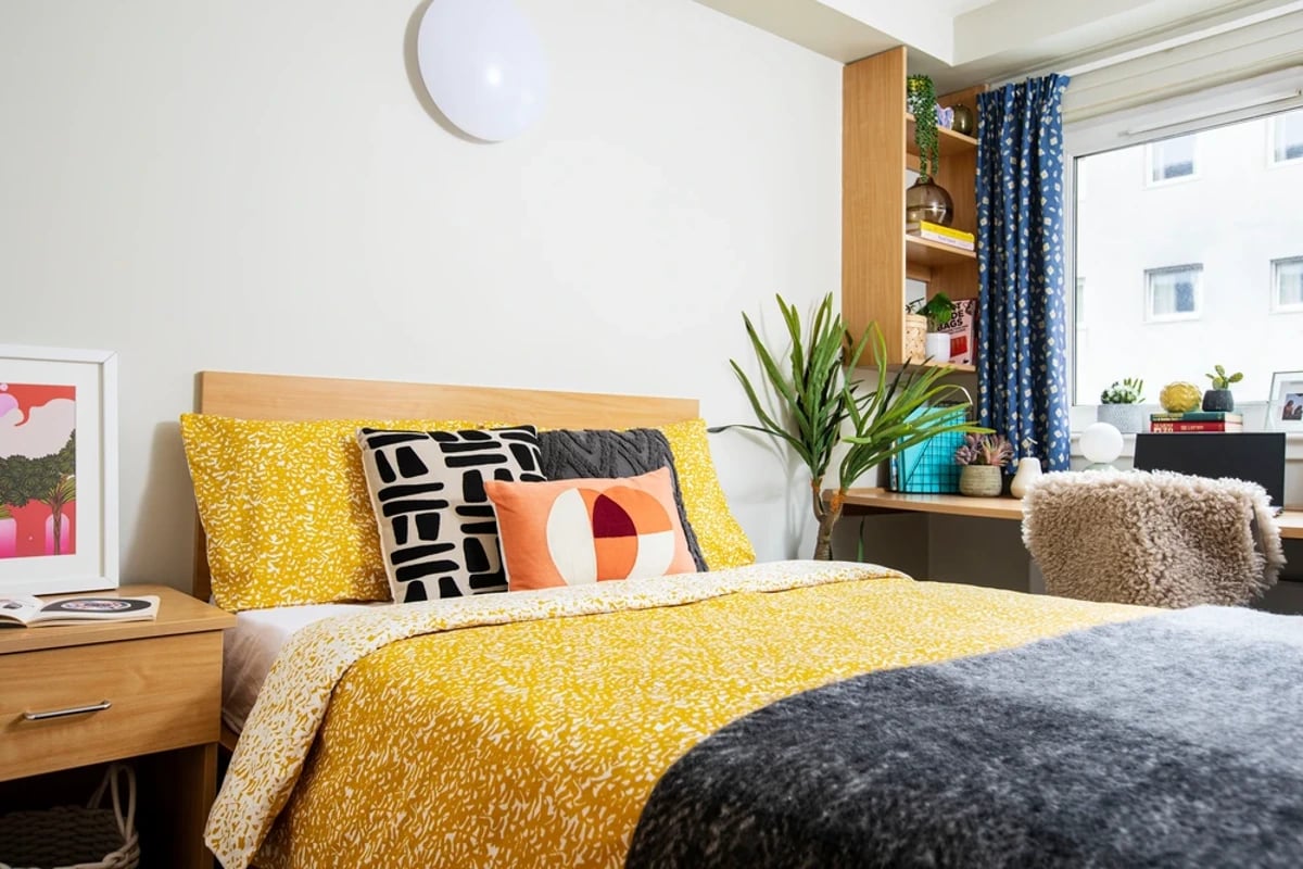 Bed with yellow patterned bedding and pillows study area at Kyle Park House in Glasgow Student Accommodation