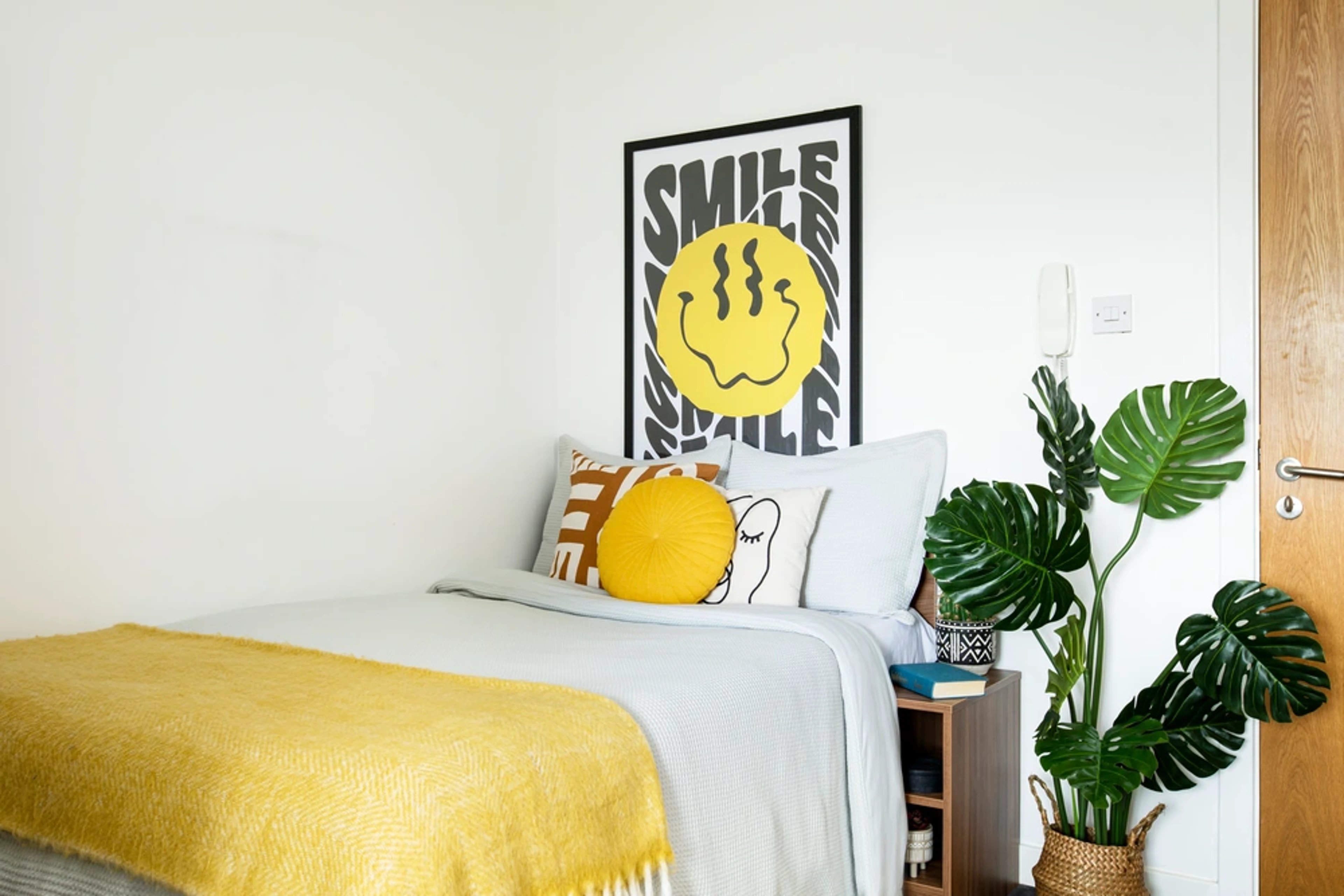 Bed with yellow blanket smiley poster Monstera plant Bedroom at Kyle Park House in Glasgow Student Accommodation