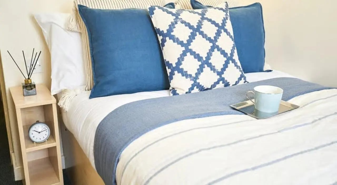 Bed with blue pillows and alarm clock Bedroom at College Court in Stoke-On-Trent Student Accommodation