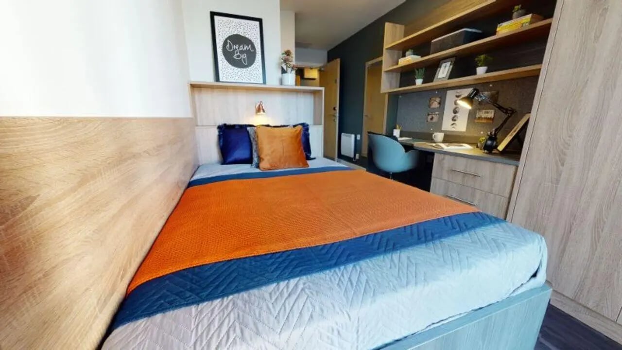 Bed with orange blue covers study desk and shelves bedroom at iQ Abacus House in Brighton Student Accommodation