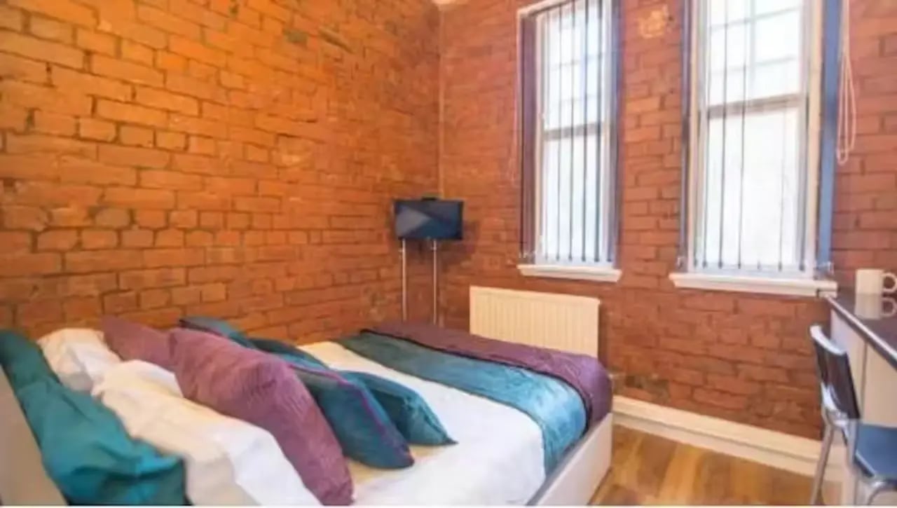 Bed with colorful pillows brick wall and TV bedroom at Ashton House in Manchester Student Accommodation