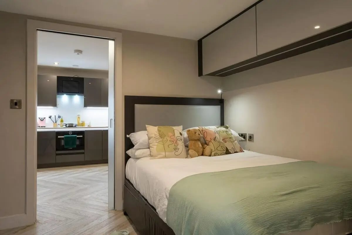 Bed with teddy bear and kitchen visible bedroom at dwell 121 Princess Street in Manchester Student Accommodation