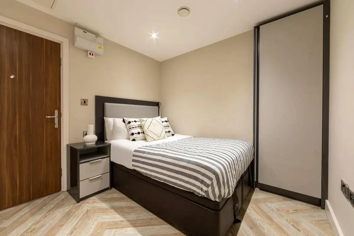 Bed with striped duvet bedside table and wardrobe bedroom at dwell 121 Princess Street in Manchester Student Accommodation