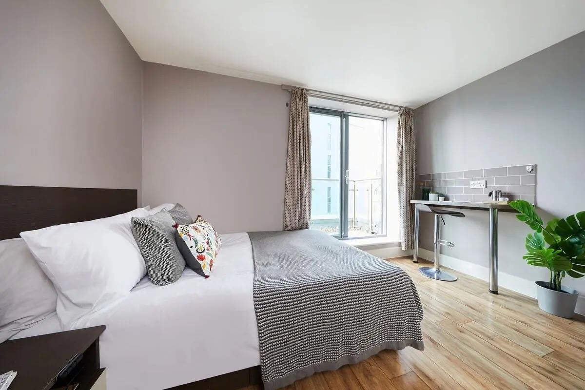 Bed with patterned pillows and desk study area at Collegiate Dashwood Studios in London Student Accommodation