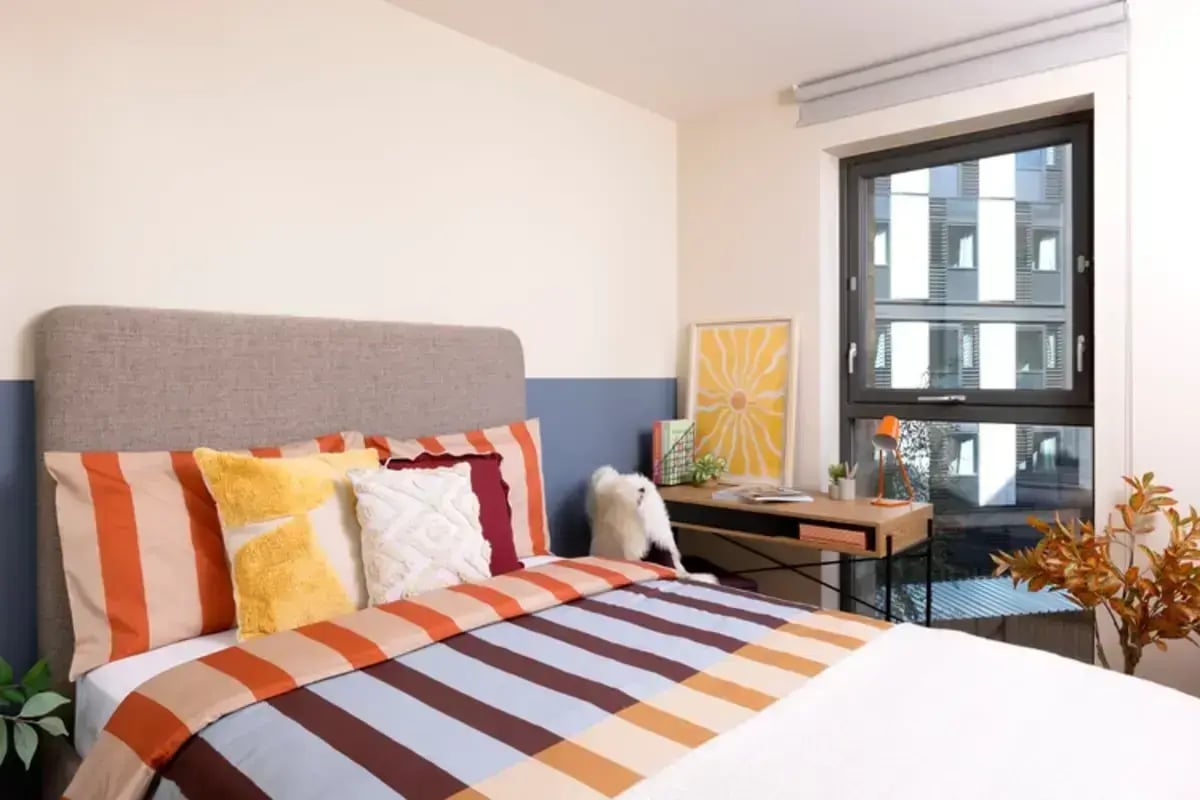 Bed with striped bedding desk lamp artwork and window bedroom at Burnet Court in Edinburgh Student Accommodation