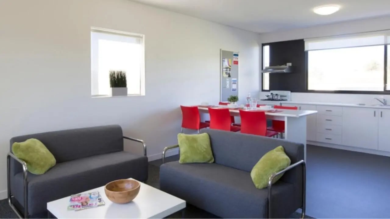 Two gray sofas with green pillows living area kitchen at Western Sydney University Campbelltown Village in Sydney Student Accommodation
