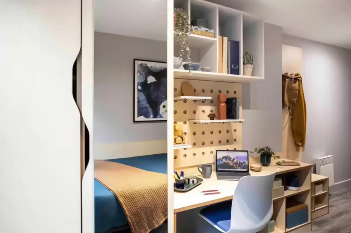 Bed with blue covers and desk with laptop Bedroom study area at Aster House in Belfast Student Accommodation