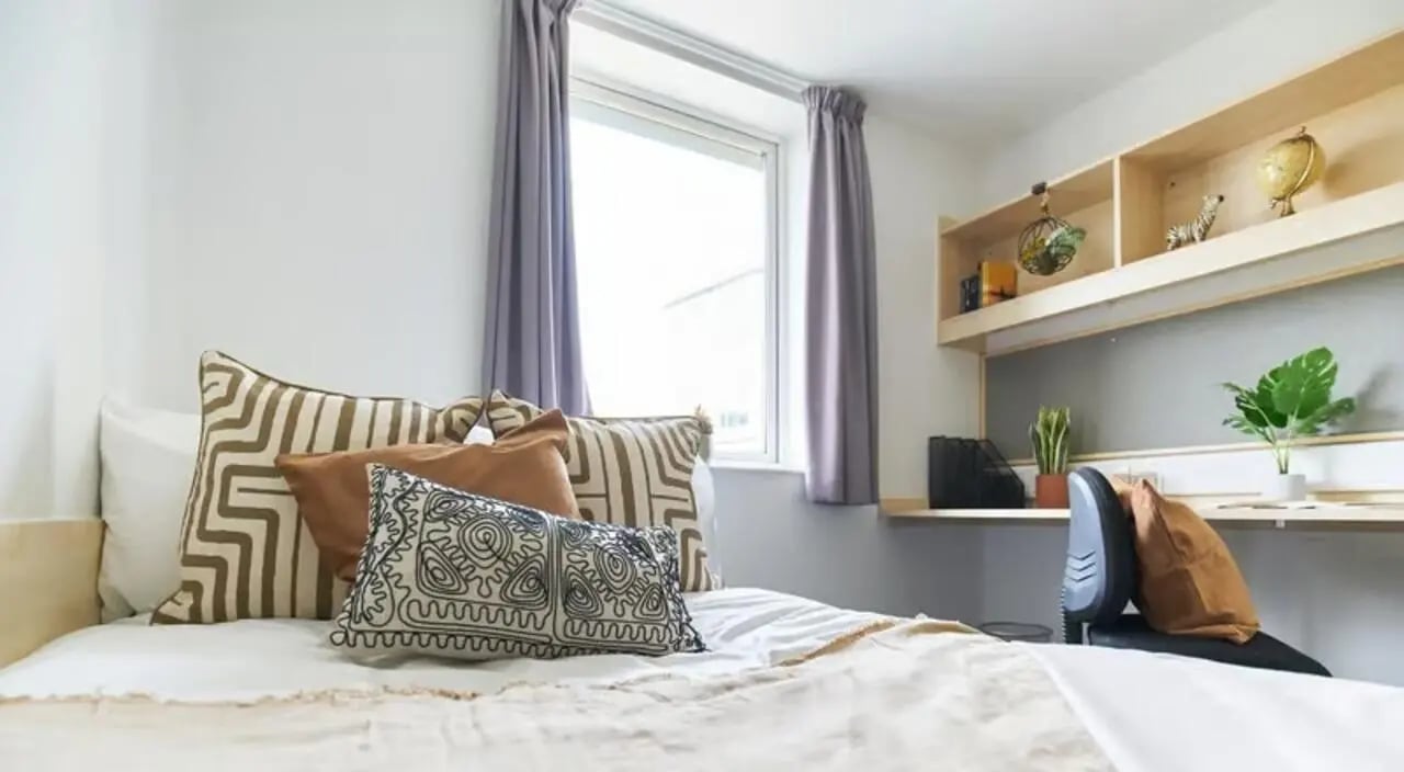 Bed pillows desk chair and shelves bedroom at The Green in Bradford Student Accommodation